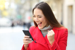 Portrait of an excited woman wearing a red coat winning on line outside on the street in winter