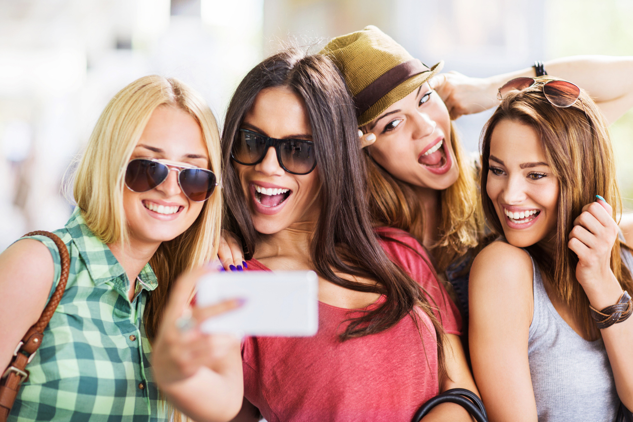 Four cheerful female friends having fun while taking a selfie with smart phone.