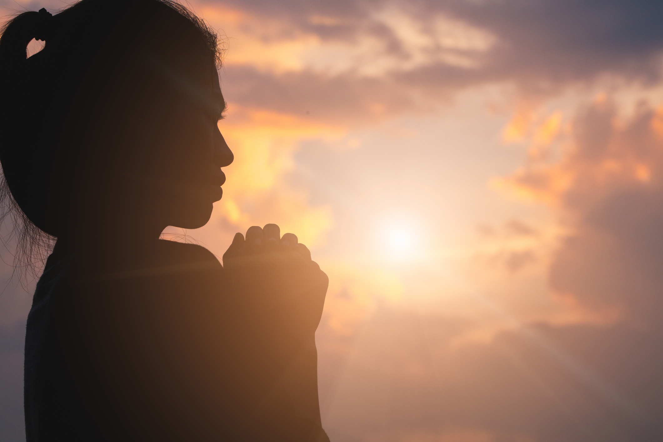 Silhouette of young human hands praying to God at sunrise, Christian Religion concept background.