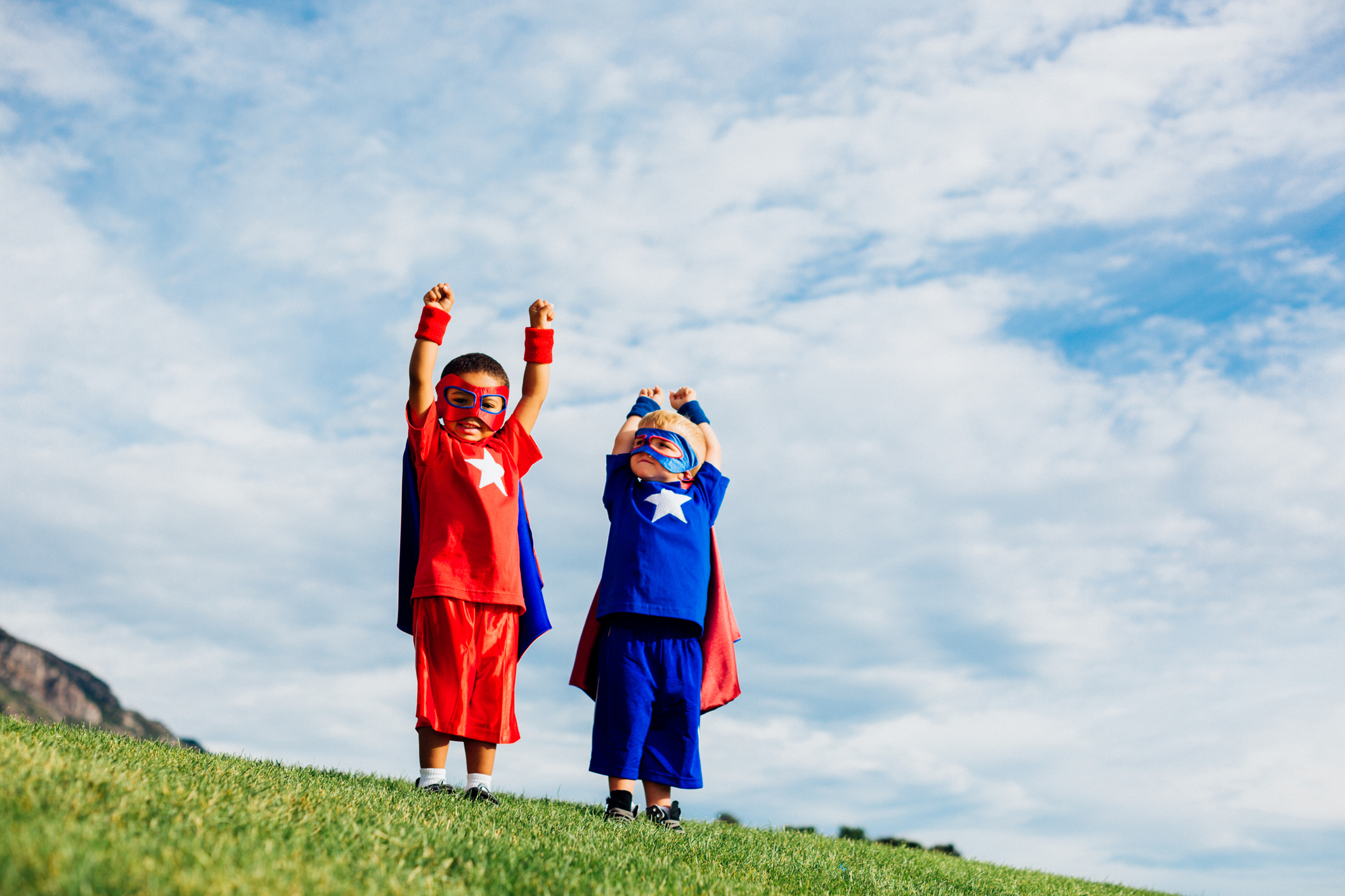 Two young boys, dressed up as superheroes, and ready to conquer their fears and show their strength in life. They are standing in a public park during summer.