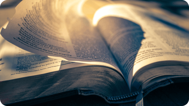 The Bible in contrasting yellow-orange and blue lighting. A page is being flipped. It is a close-up view
